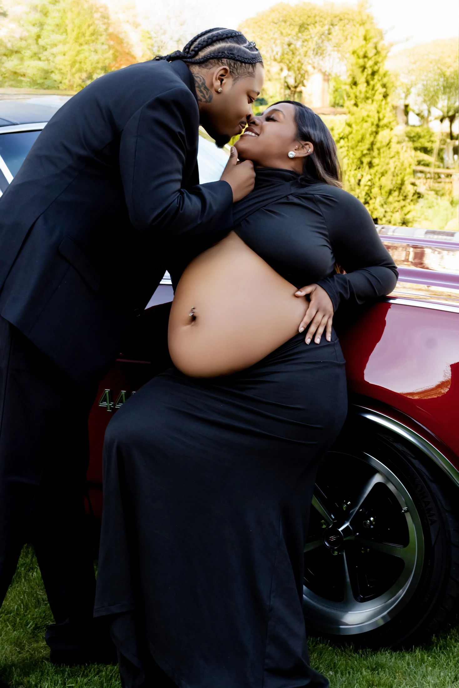 Expectant parents in black posing beside a classic car